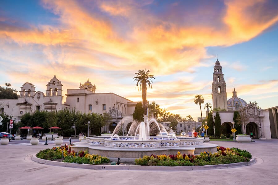 As the sun sets, casting a radiant orange glow over San Diego, the enchanting Balboa Park comes alive with twinkling lights reflecting off the central fountain.