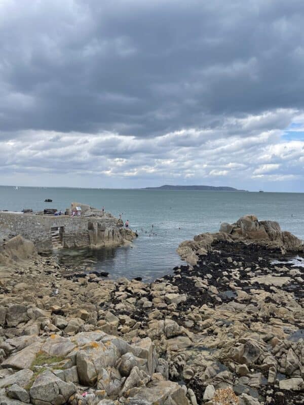 A rock beach in Dun Laoghaire, with people swimming in the water