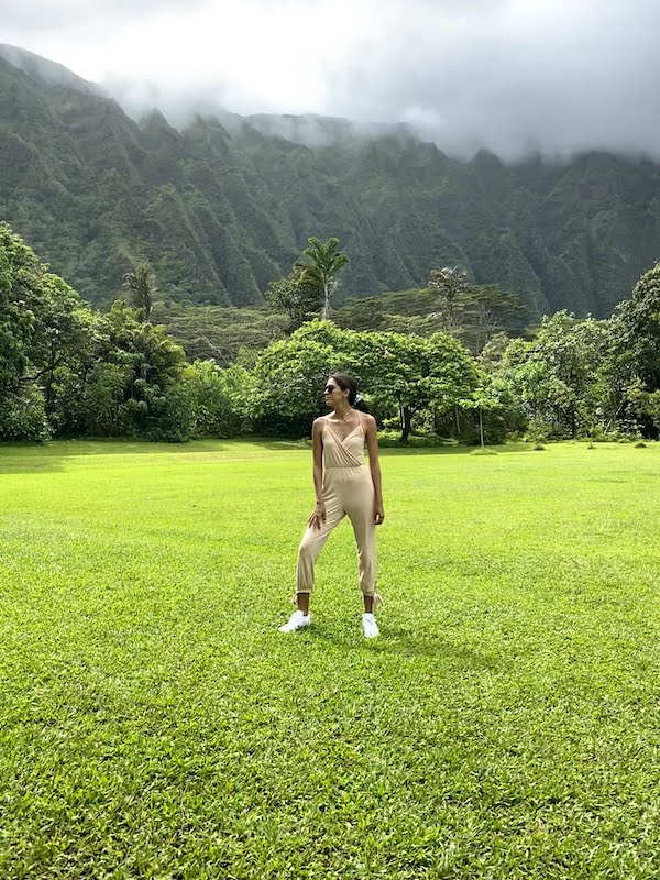 A girl standing in the grass in Hoʻomaluhia Botanical Garden, with lush green trees in the background