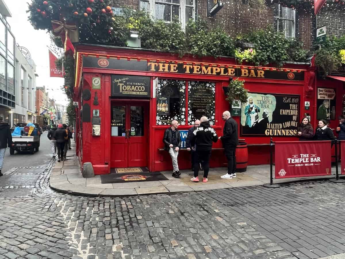 The iconic red exterior of The Temple Bar pub in Dublin, Ireland, adorned with festive decorations, as locals and tourists mingle on the cobbled streets