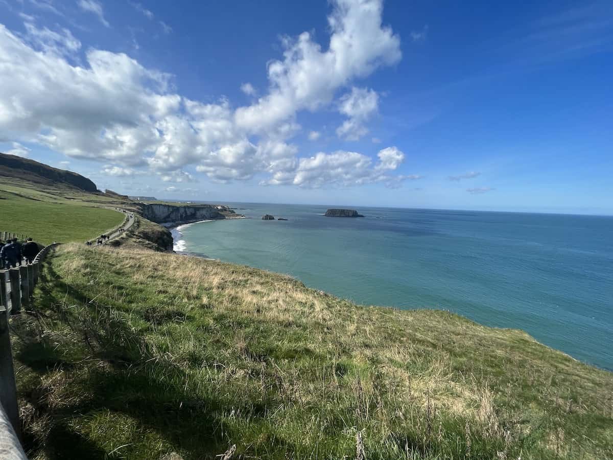 Breathtaking view of the rugged Irish coastline with rolling green hills and cliffs overlooking the vast blue sea under a sky dotted with fluffy clouds